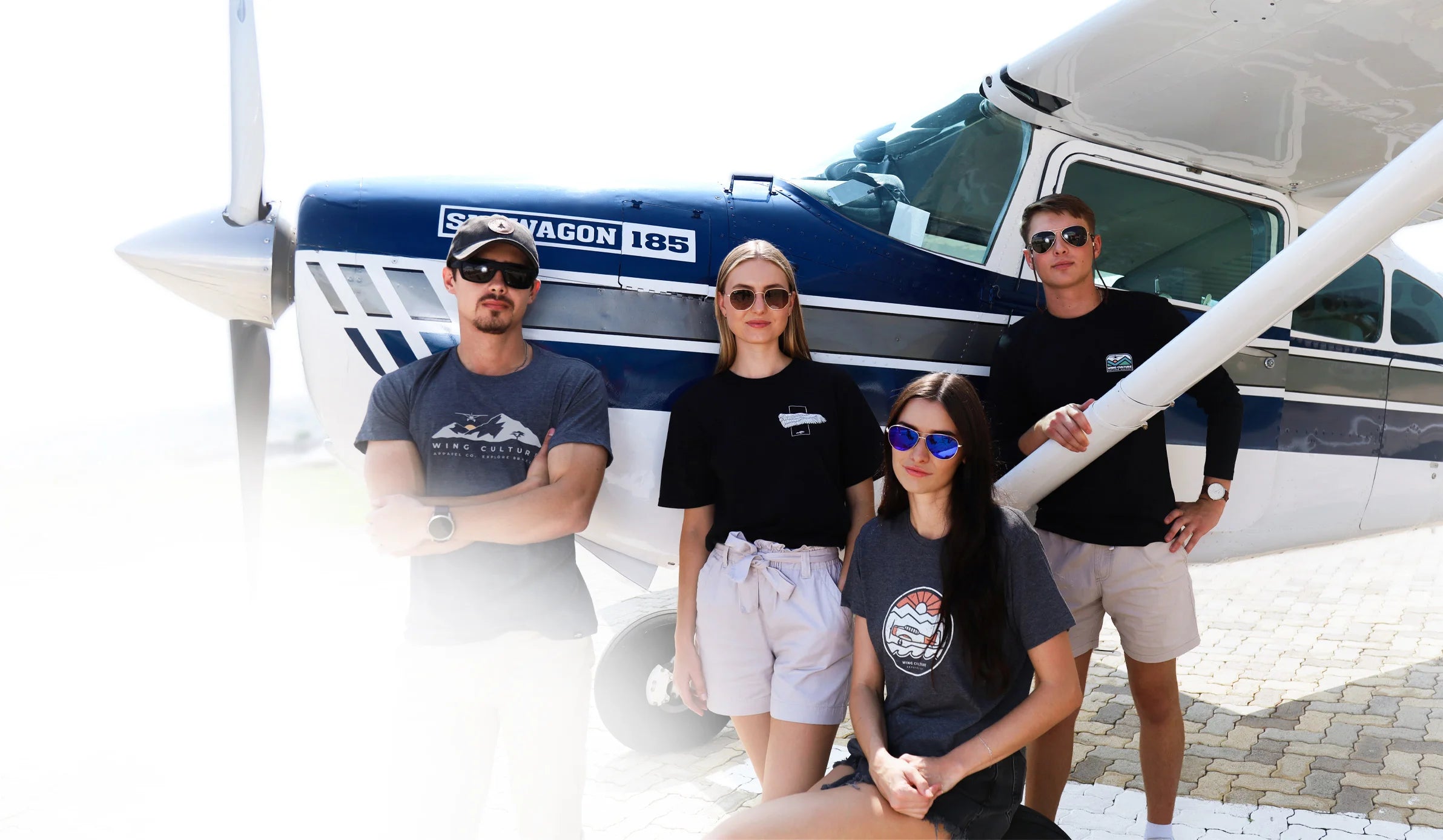 Four people posing in front of a small airplane wearing Wing Culture aviation apparel